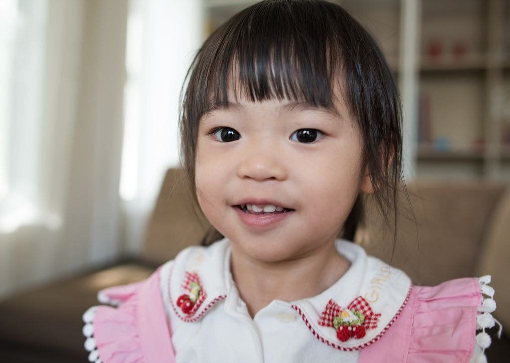 A little asian girl showing late symptoms of when do babies start teething.